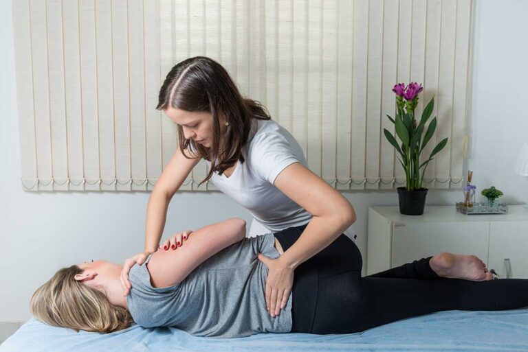 A chiropractor gently assessing the knee of an athletic adult on an exam table.