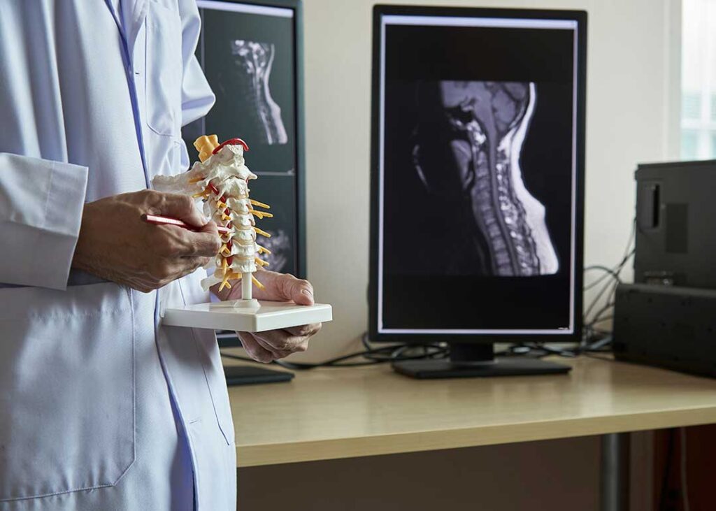A clinician discusses back pain with an adult patient beside an examination table.